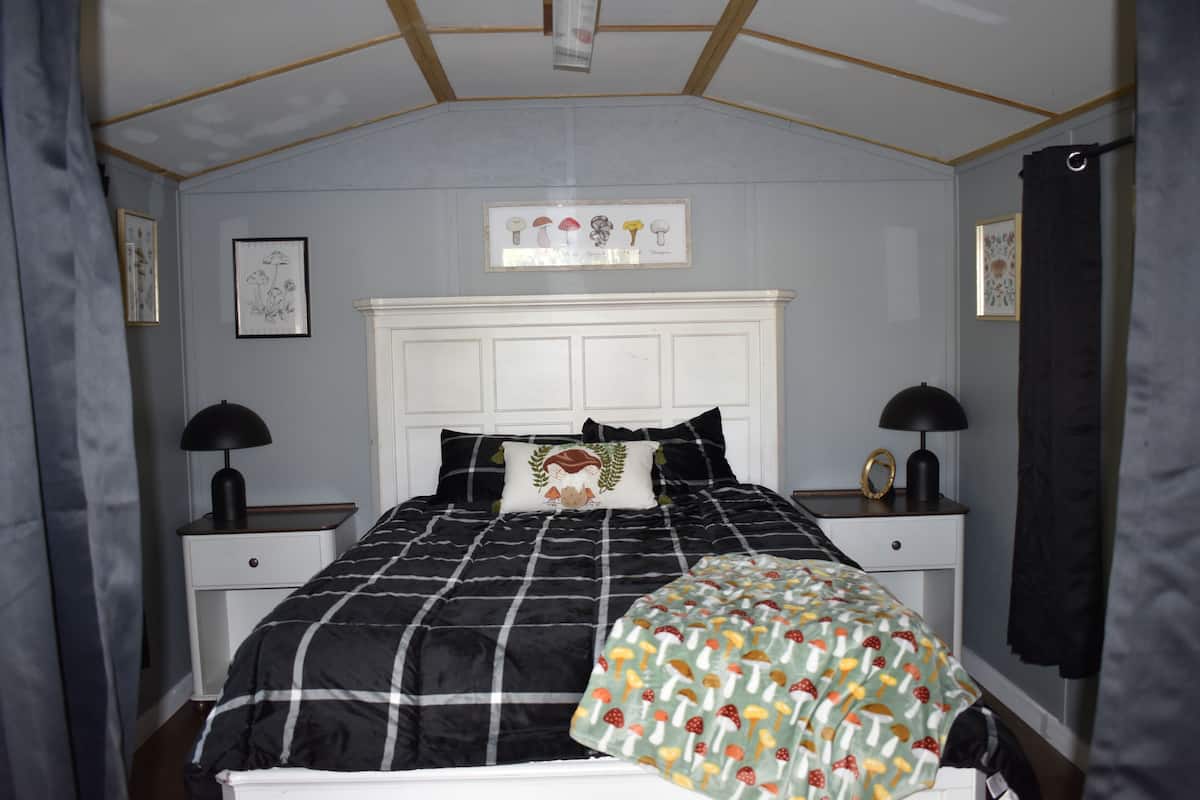 A bedroom with a bed, two bedside tables, a headboard, and a wall-mounted picture.