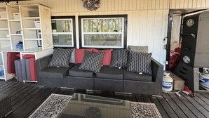 A cozy living area with a dark-colored sofa, patterned cushions, and a decorative wall hanging. There are two windows providing natural light, and a ceiling fan overhead. - RAINBOW RANCH CABINS (Dunnellon)