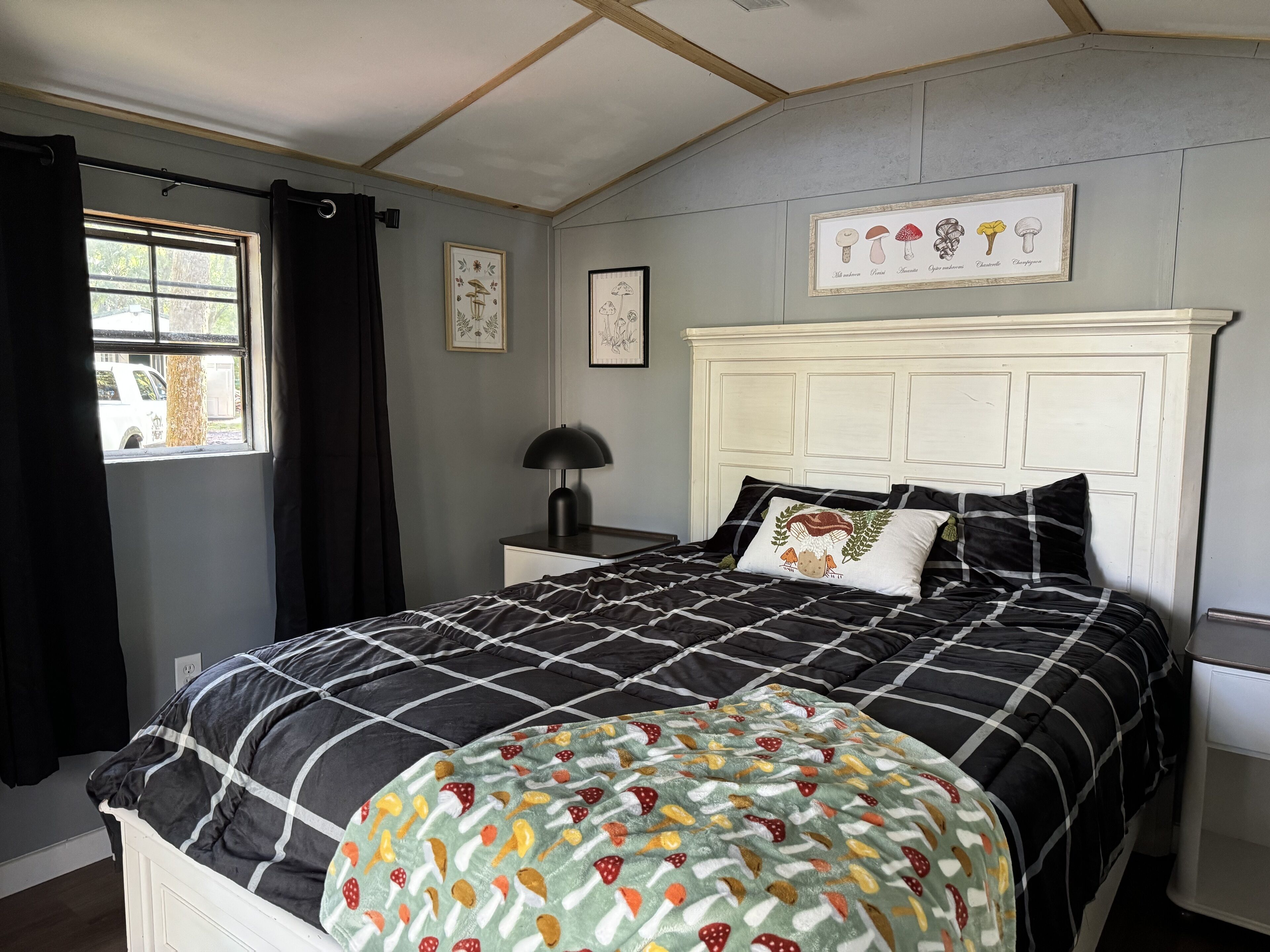 Un dormitorio con cama, mesita de noche, lámpara, ventana con cortinas y decoración en la pared.