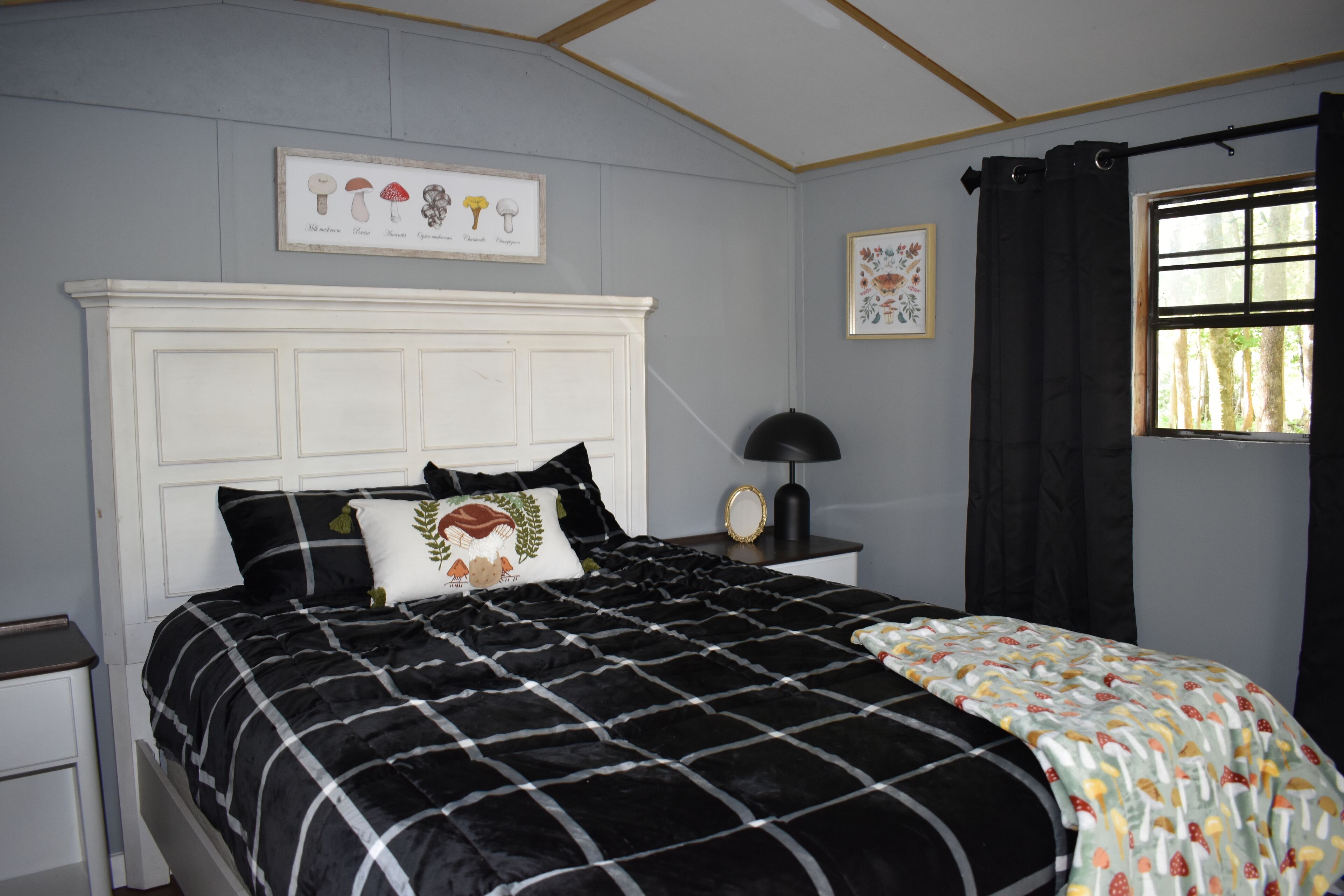 Un dormitorio con cama, mesita de noche, lámpara de pared y ventana con cortinas.