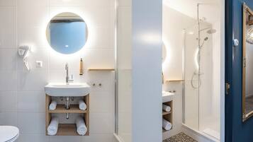 A modern bathroom with a white sink, a mirror, a shower, and a toilet.