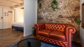 A room with a brown leather sofa, a bed, a stone wall, and a small table with a plant.