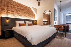 A modern bedroom with a brick wall, a large bed with white bedding, a desk with a chair, and a large mirror. - Grapèlli Boutique Hotel (Alkmaar)