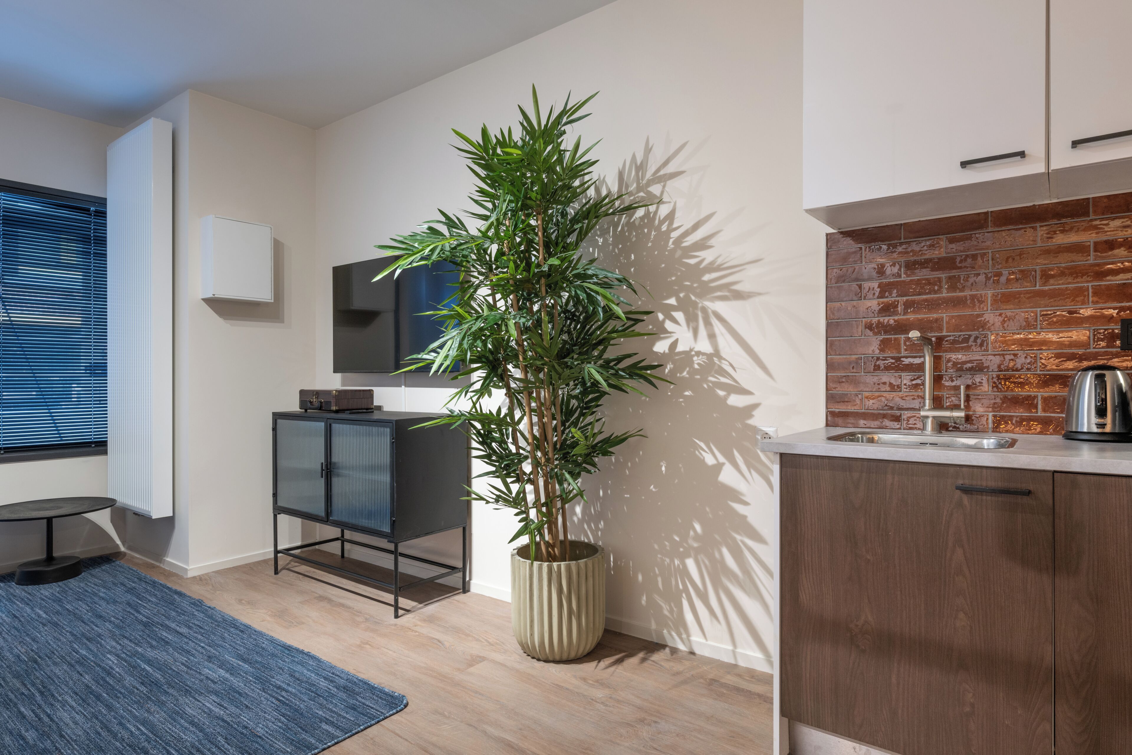 A modern kitchen with a brick backsplash, a potted plant, and a small dining area with a table and chairs.