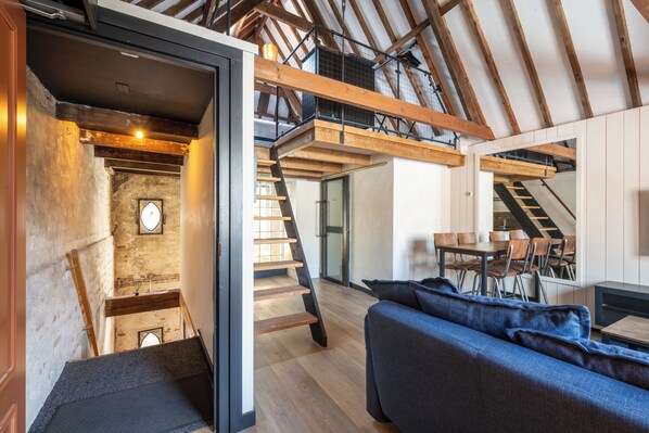A modern interior with a staircase leading to a loft area, a dining table with chairs, and a blue sofa. - Grapèlli Boutique Hotel (Alkmaar)