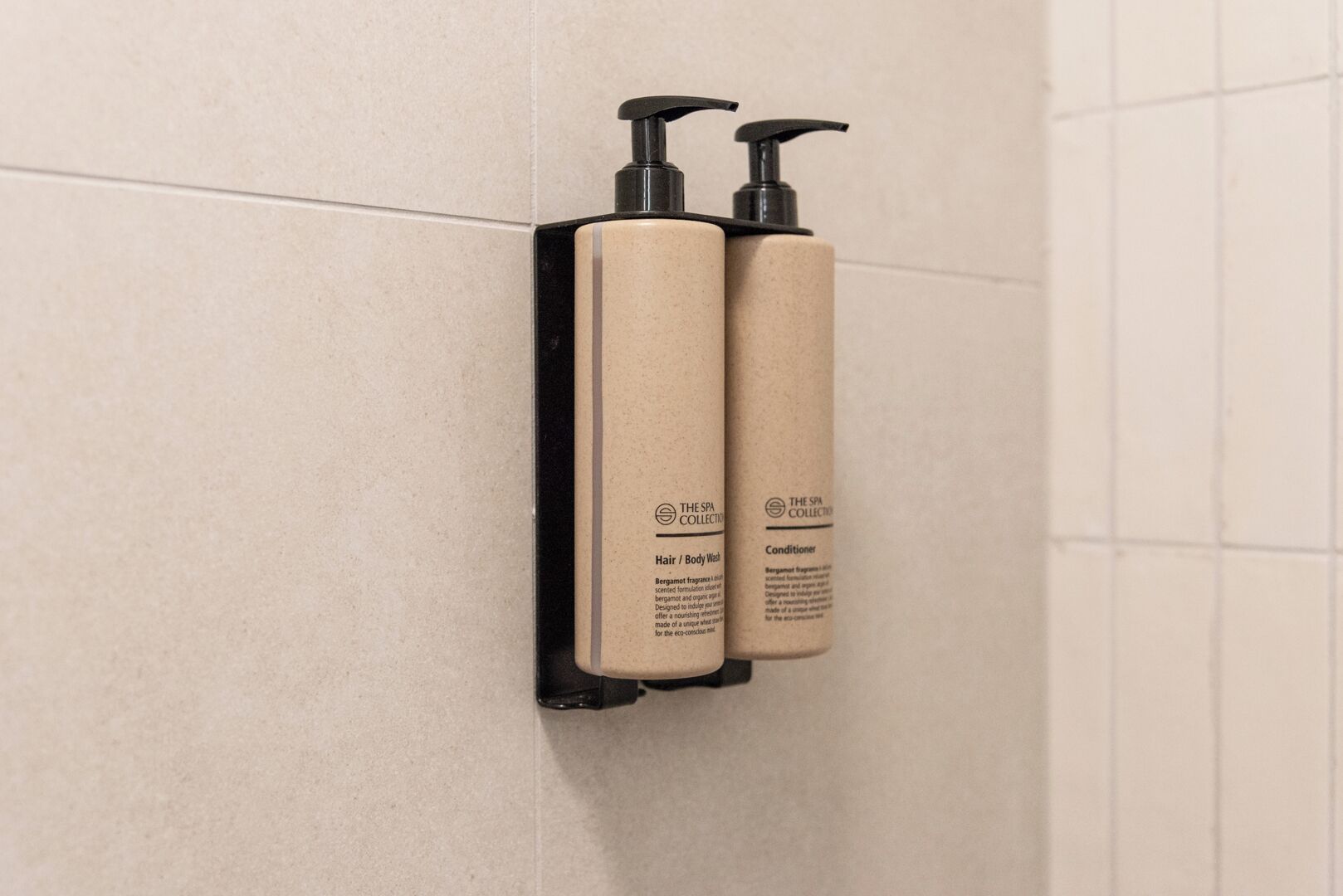 Zwei Flaschen aus der Spa-Linie an einer Wand angebracht, eine mit dem Aufdruck 'Haar- und Duschgel' und die andere 'Spülung'.