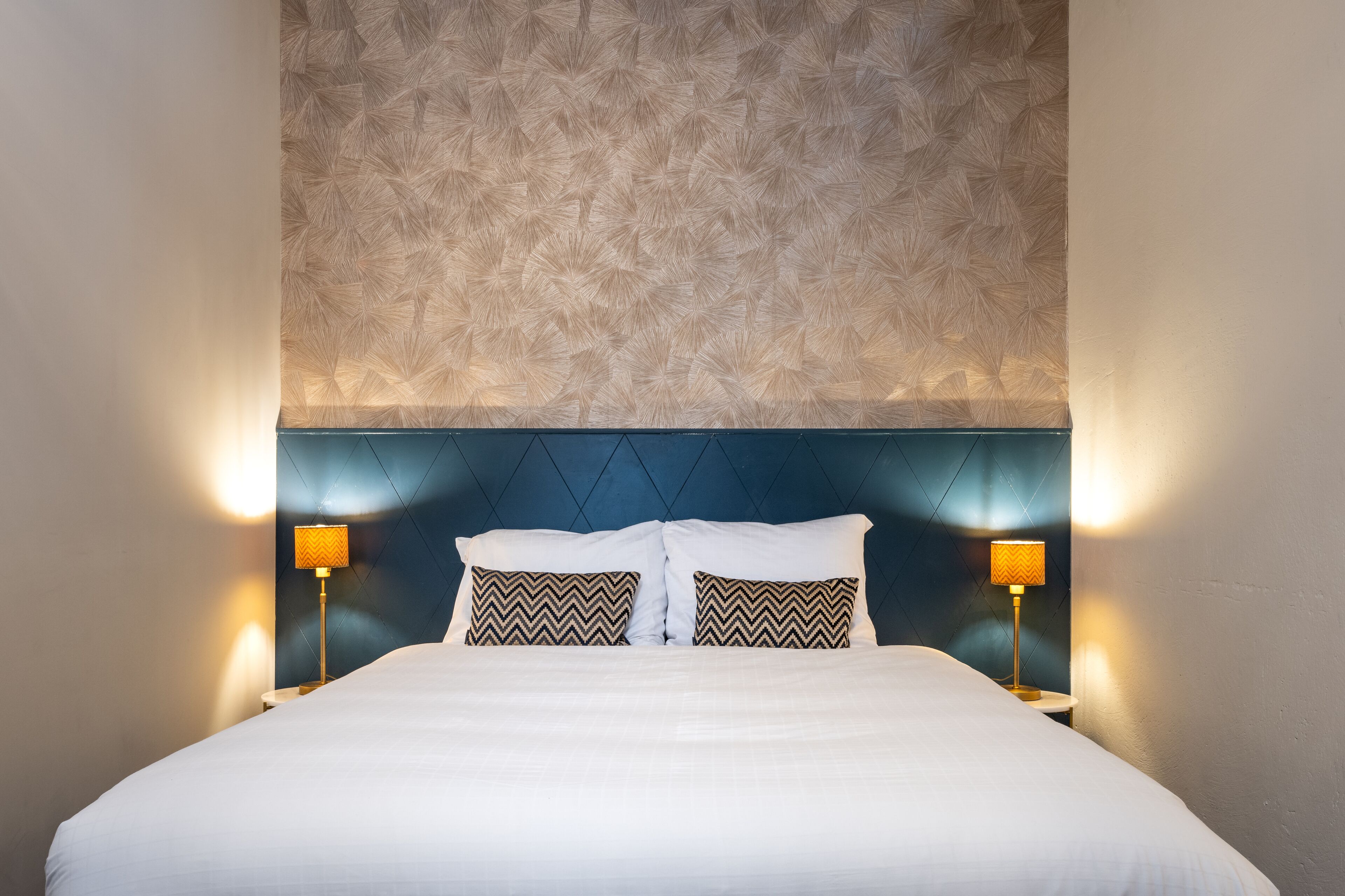 A neatly made bed with two pillows, a textured ceiling, and two bedside lamps.