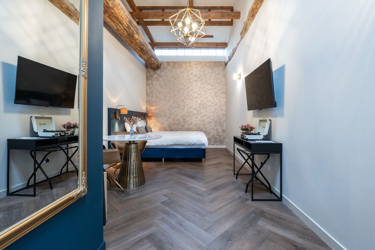 A bedroom with a bed, a desk, a chair, a TV, and a large mirror.