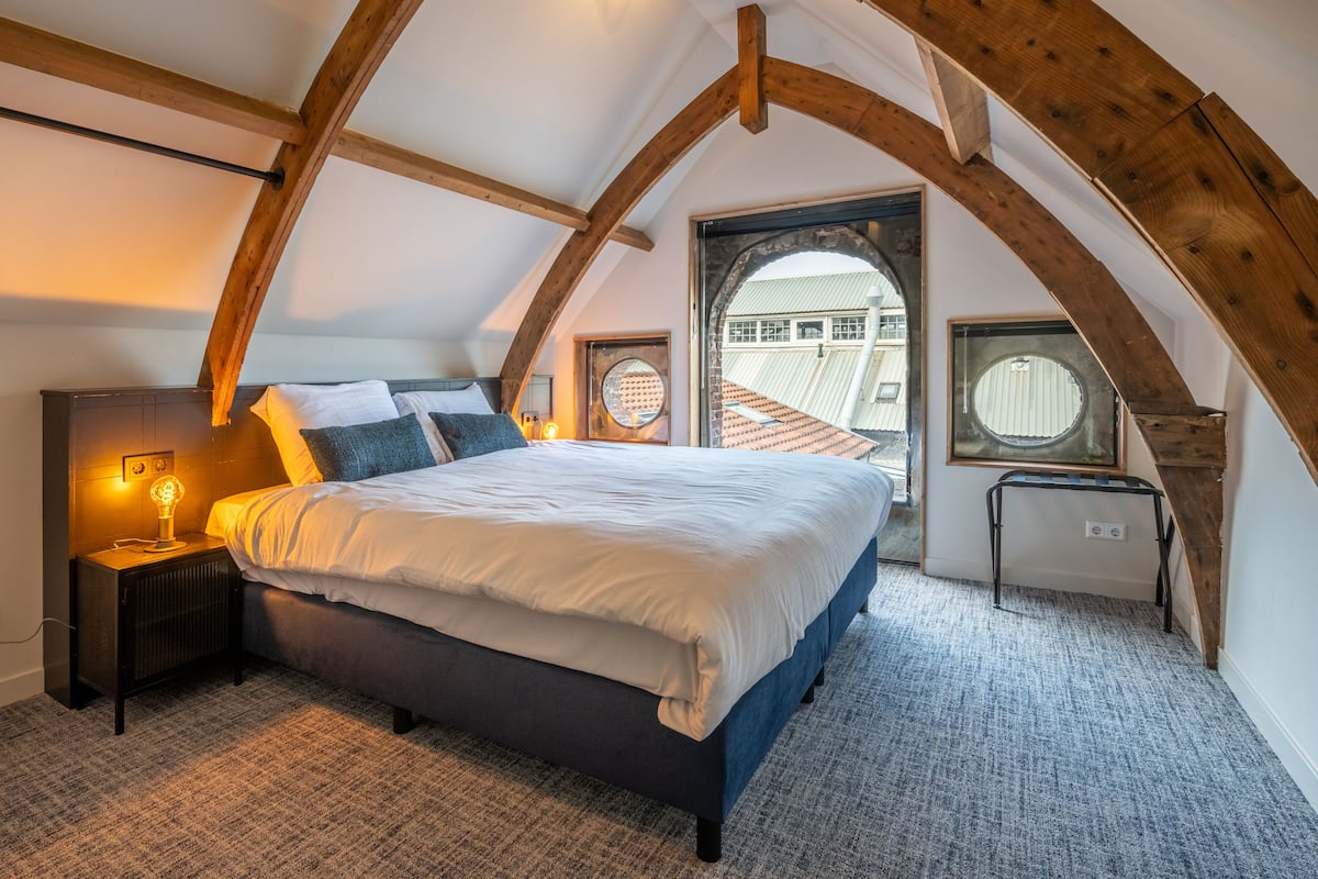 A bedroom with a bed, a nightstand, a window, and a view of the outside.
