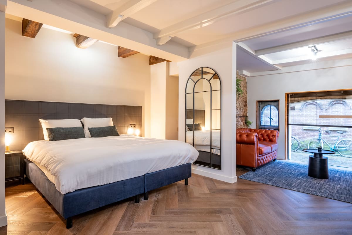 A modern bedroom with a large bed, a mirror, a leather sofa, and a view of the outside.