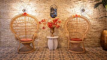 Two wicker chairs with cushions, a small table with a vase of flowers, and a brick wall with a sign.