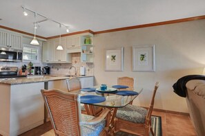 A modern kitchen with white cabinets, a central island, and a dining area with wicker chairs and a glass table.