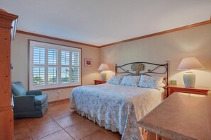 A bedroom with a bed, two bedside tables, a chair, a window with blinds, and a view of greenery outside. - Ground Floor, Ocean views, steps from the sand, High end vacation home (Saint Augustine Beach Florida)