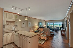 A kitchen with a central island, dining area with wicker chairs, and a view of the ocean through large windows.