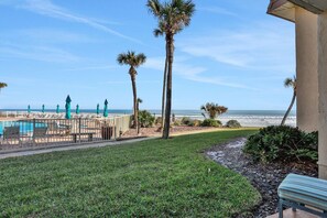 A pool area with lounge chairs and umbrellas, palm trees, and a view of the ocean. - Ground Floor, Ocean views, steps from the sand, High end vacation home (Saint Augustine Beach Florida)