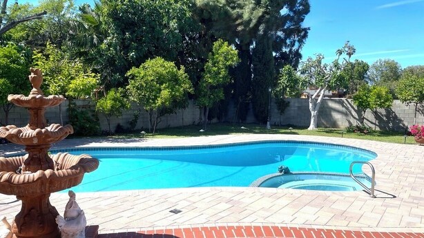 A swimming pool with a fountain, surrounded by a brick patio and trees. - Comfy & Inviting Poolside Casita near Bike Path (Los Angeles)