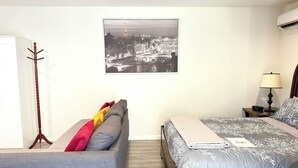 A bedroom with a bed, a sofa, a coat rack, a nightstand, a lamp, and a framed picture on the wall. - Comfy & Inviting Poolside Casita near Bike Path (Los Angeles)