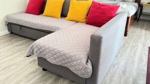 A grey sofa with a quilted cover, a wooden floor, and a bed with grey bedding in the background. - Comfy & Inviting Poolside Casita near Bike Path (Los Angeles)