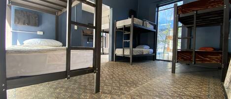 A dormitory room with bunk beds, patterned floor tiles, and a window with a view of the outside.