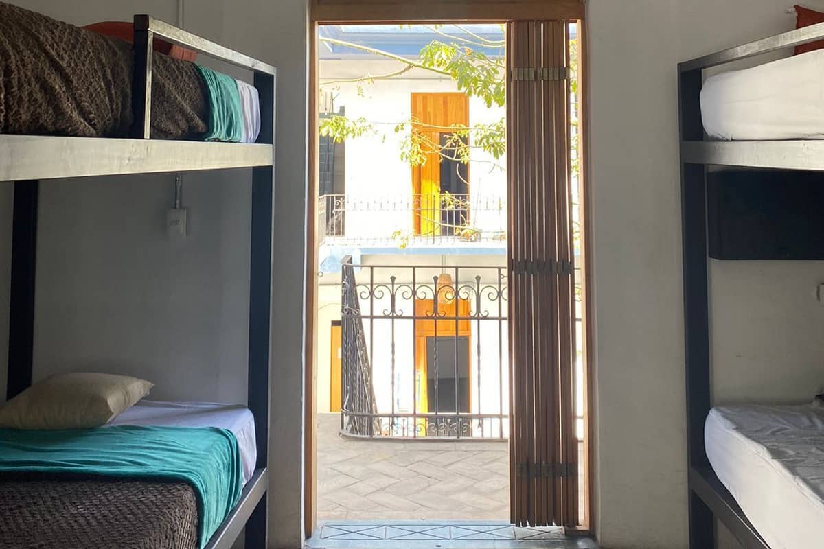 Une chambre de dortoir avec des lits superposés, une petite fenêtre et une porte donnant sur un balcon extérieur.
