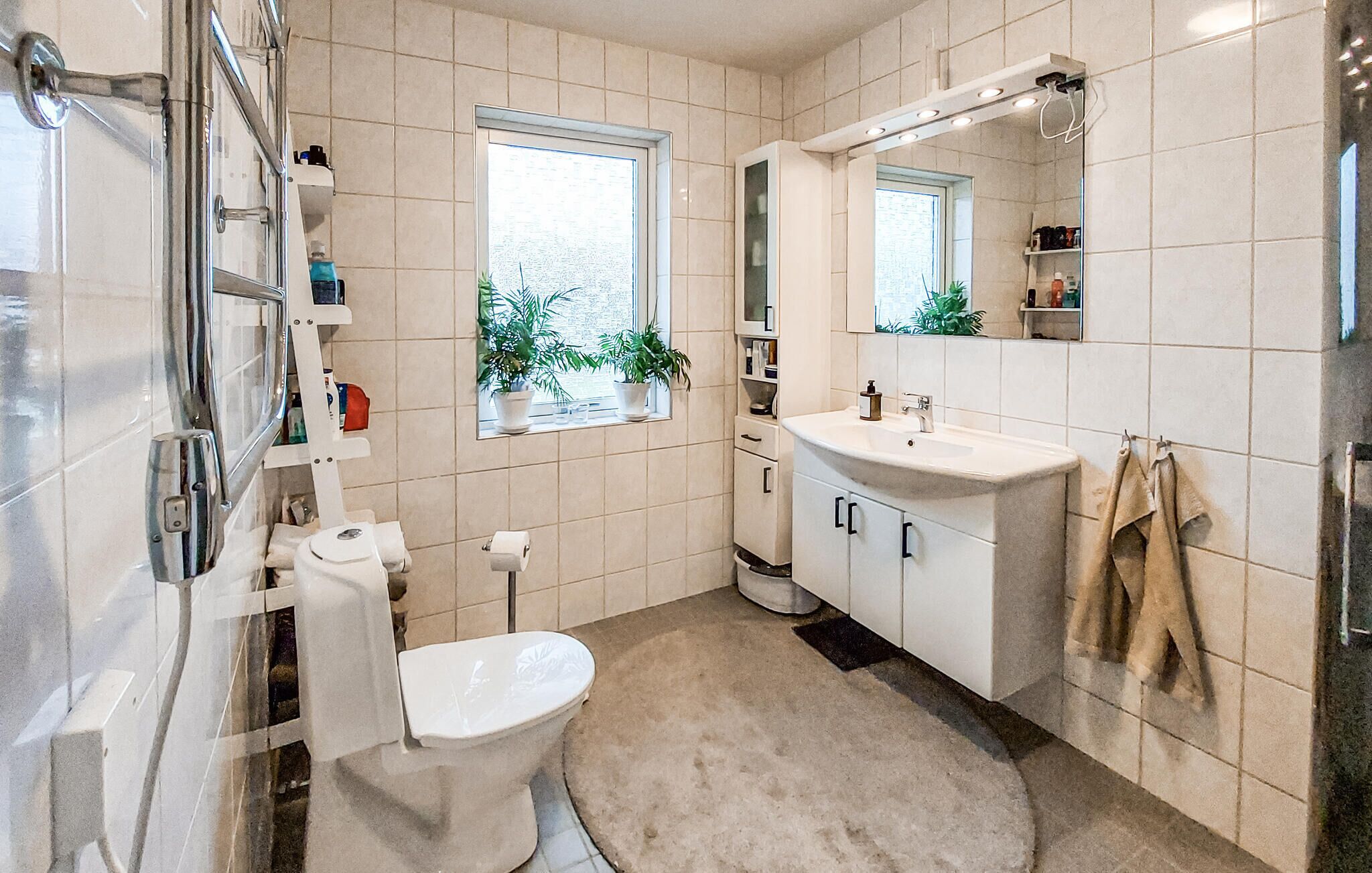 A bathroom with a toilet, sink, mirror, and potted plants.