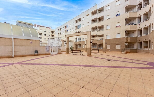 A courtyard with tiled flooring, a central seating area, and a building with multiple balconies and windows.