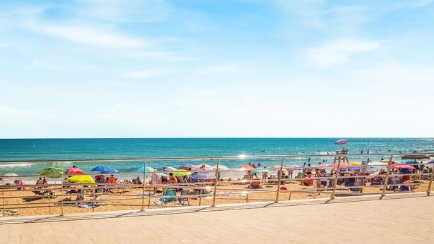 A beach with a clear sky, a sandy shore, and people enjoying the water. - Cozy apartment in Torrevieja with swimming pool (Torrevieja)