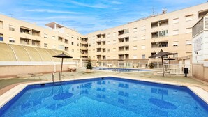 A swimming pool with a tiled deck, surrounded by a multi-story building with balconies and a covered area. - Cozy apartment in Torrevieja with swimming pool (Torrevieja)
