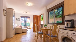 Una cocina compacta con lavadora, una zona de comedor con sillas y mesa, y un ventanal corredero que da a un balcón.