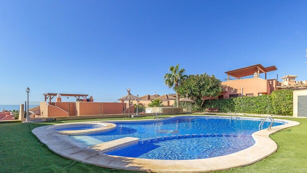 Una piscina de borde curvo, rodeada por un césped bien cuidado y un edificio de techo plano al fondo.