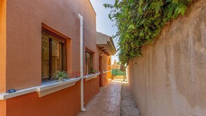 Un callejón estrecho con un edificio a un lado y una pared con vegetación al otro.