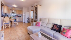 Un espacio habitable compacto con kitchenette, comedor y sofá con almohadones decorativos.