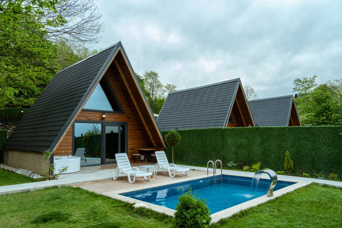 A modern villa with a swimming pool, two lounge chairs, and a small patio area.
