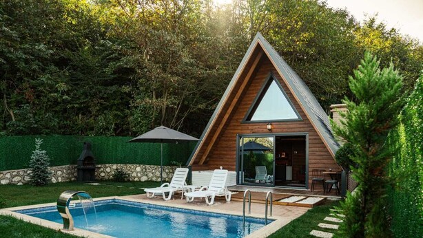 Una moderna casa a forma di A con piscina, area salotto esterna e un muro in pietra.