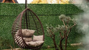Una poltrona sospesa con cuscini in un giardino con un siepe ben curata sullo sfondo.