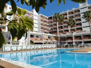 A modern hotel with multiple balconies, a swimming pool, and palm trees. - Holiday Home Sea Breeze (Playa del Inglés)