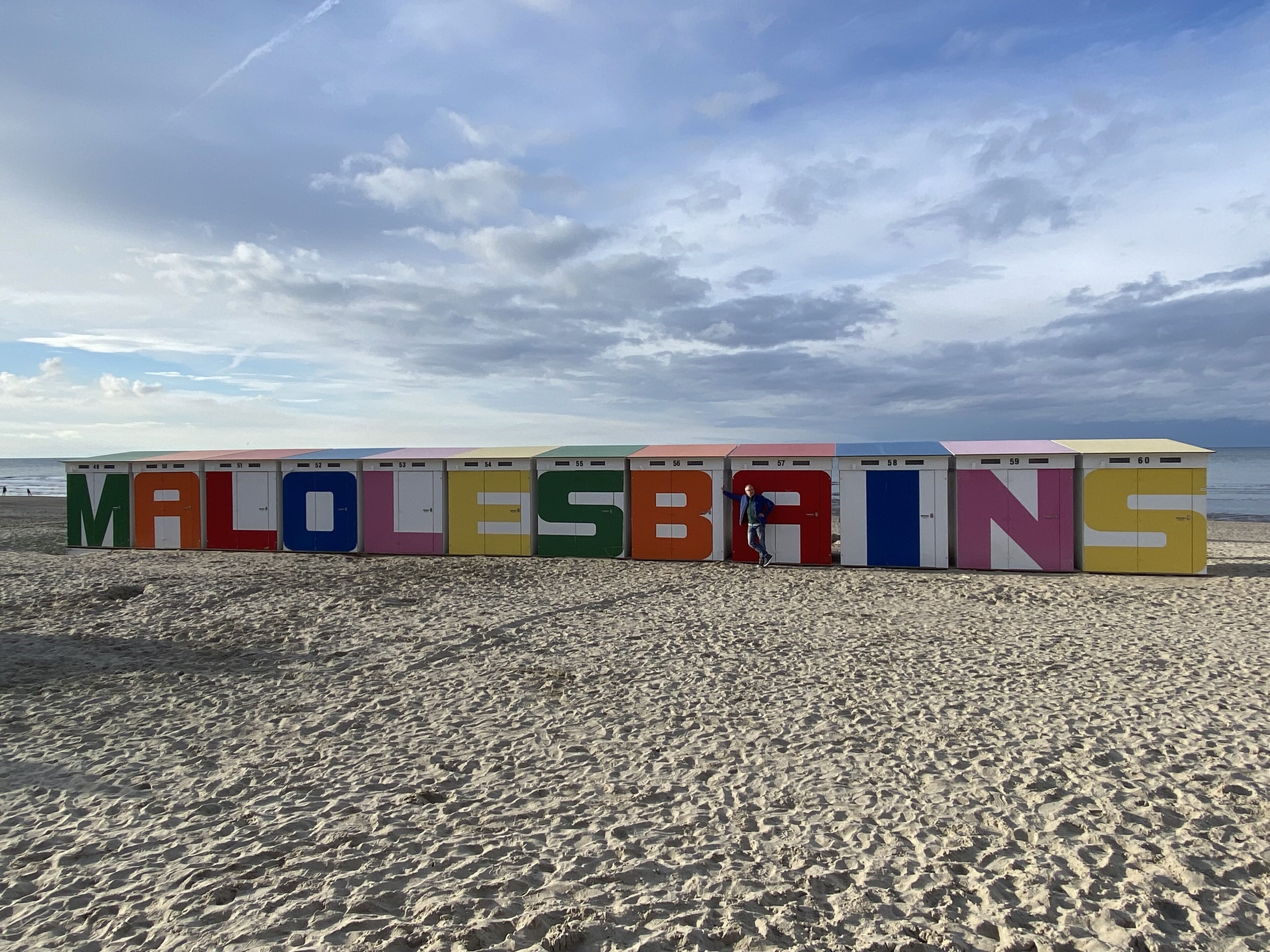 Een rij kleurrijke strandhutten met nummers, met de tekst 'MALLESBRINS' op de zijkant.
