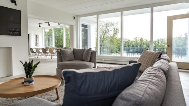 Ein geräumiges Wohnzimmer mit großem Fenster, einem grauen Sofa, einem runden Couchtisch und einem Essbereich im Hintergrund.