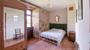 A bedroom with a stone wall, a wooden wardrobe, a bed with a white bedspread, a green headboard, and a small bedside table. - Lake front home in Chiché with house sea view (Chiché)