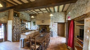 A rustic kitchen with a stone wall, wooden beams, a long wooden table, and a tiled floor. - Lake front home in Chiché with house sea view (Chiché)