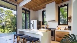 Una cocina moderna con una isla grande, taburetes de bar y vistas a exuberante vegetación.