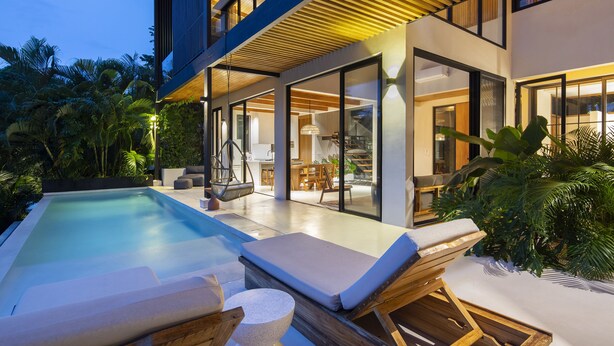 Una casa moderna con piscina, sillas de descanso y un interior bien iluminado.