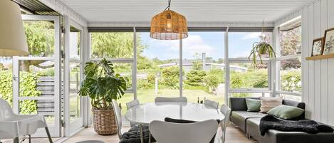 A spacious room with a large dining table, white chairs, a sofa, and a hanging light fixture.