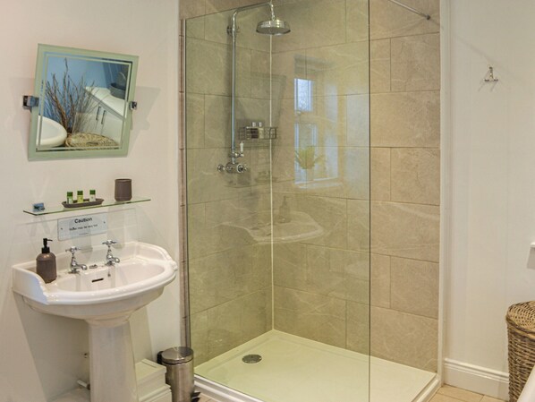 A bathroom with a glass-enclosed shower, a pedestal sink, and a small shelf with toiletries.