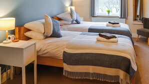Habitació d'hotel amb dos llits, una tauleta de nit amb làmpada, una cadira i una finestra amb cortines.