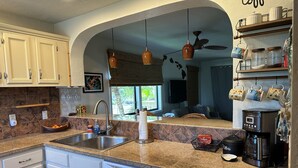 Una cocina con encimera de granito, pileta de acero inoxidable y muebles blancos. Hay una cafetera y un escurreplatos sobre la encimera.