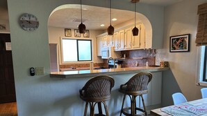 Una cocina con una isla central, dos taburetes de bar, una mesa de comedor y un reloj en la pared.