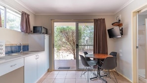 Una cocina compacta con zona de comedor, un televisor montado en la pared y un ventanal corredero que da a un espacio exterior.