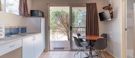A compact kitchen with a dining area, a TV mounted on the wall, and a sliding glass door leading to an outdoor area.