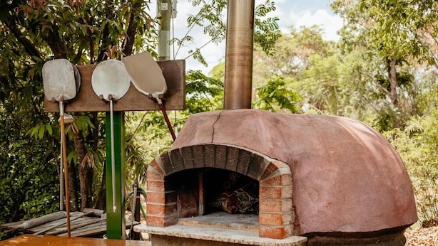 Un horno de pizza de ladrillo con un soporte de metal verde y una mesa de madera al frente.